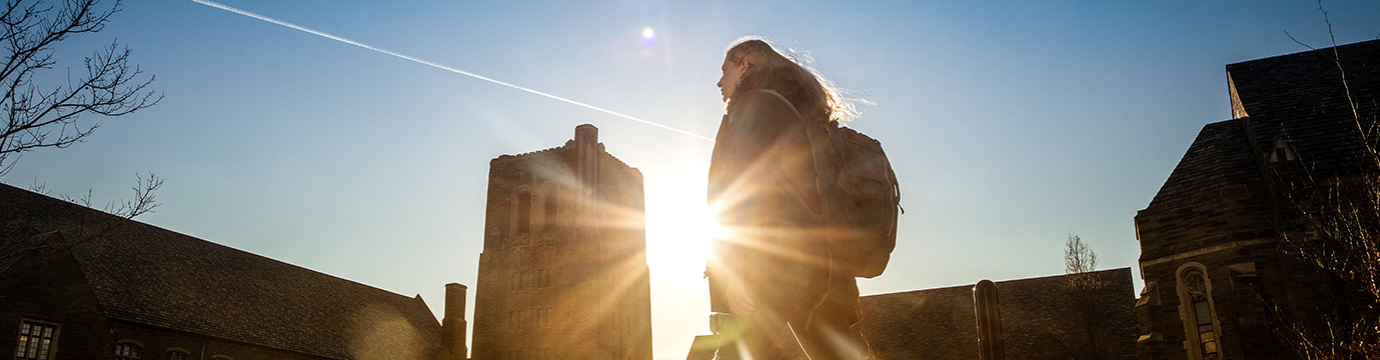 a woman walking in front of campus buildings with sunshine