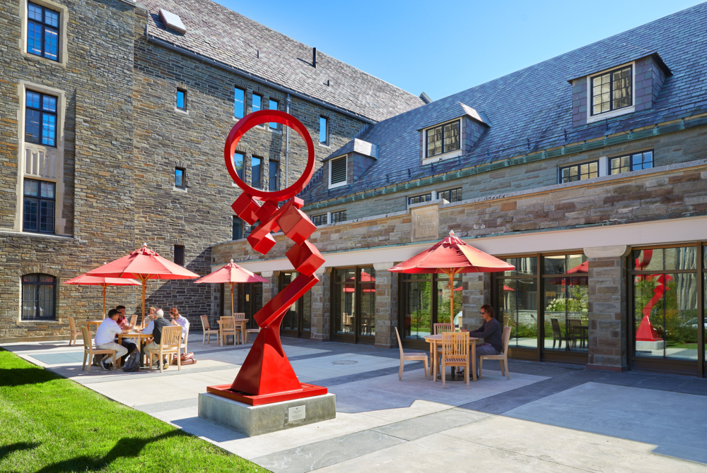 red statues and umbrellas in a courtyard with students eating at tables