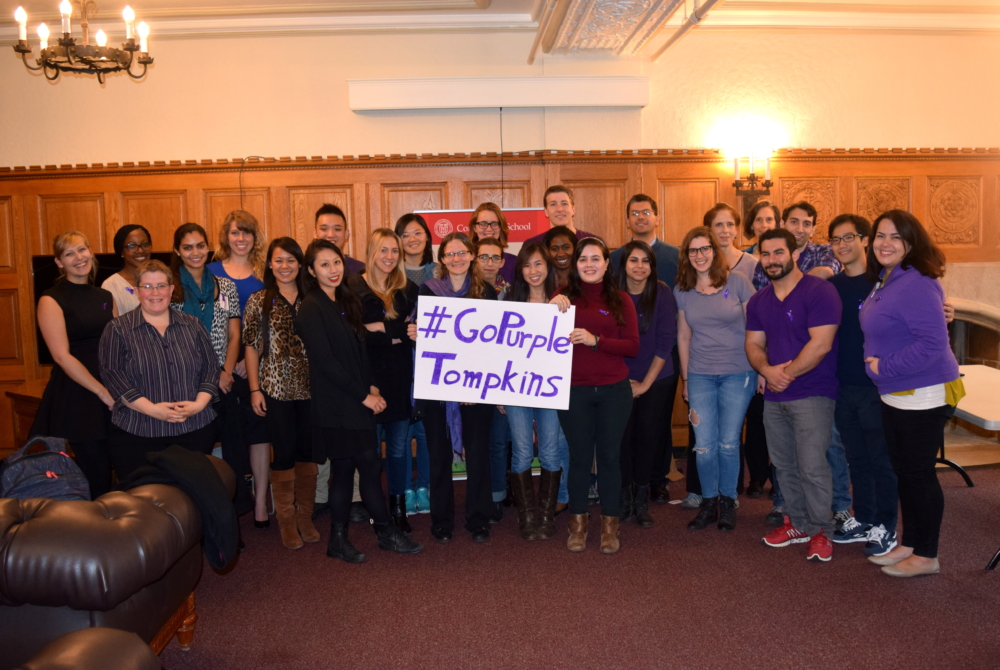 group of people with a sign saying #gopurple Tompkins