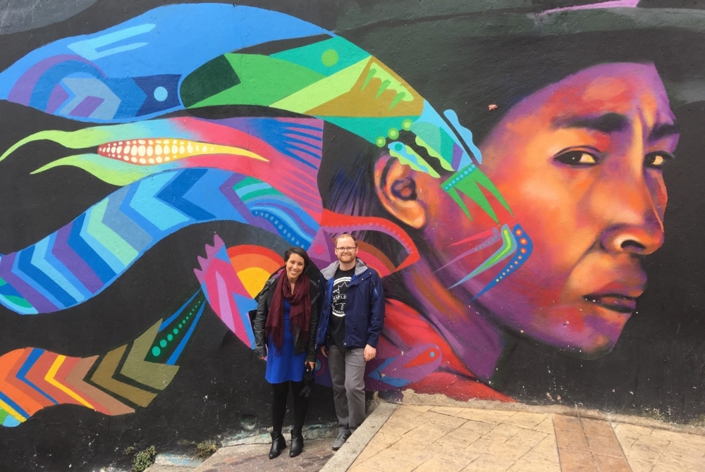 two people in front of a colorful wall mural