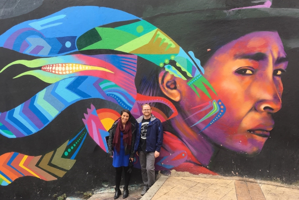 two people in front of a colorful wall mural