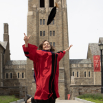 Student in full graduation regalia jumping in the air while throwing her black velvet cap