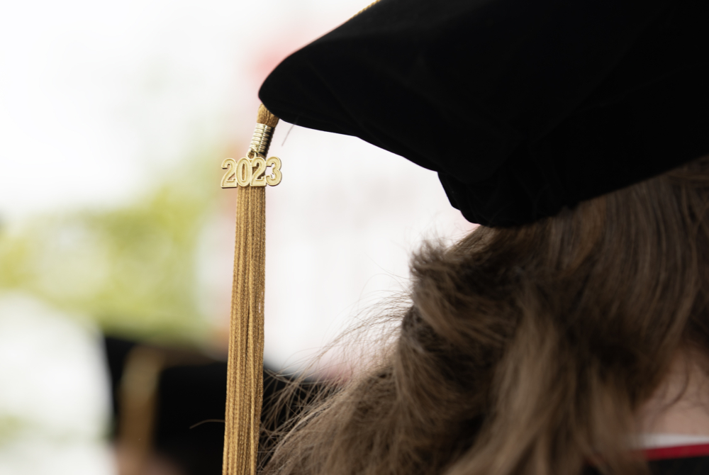 Photo of a golden tassel with 2023 in gold numbers hanging from the back of a black velvet graduation cap.
