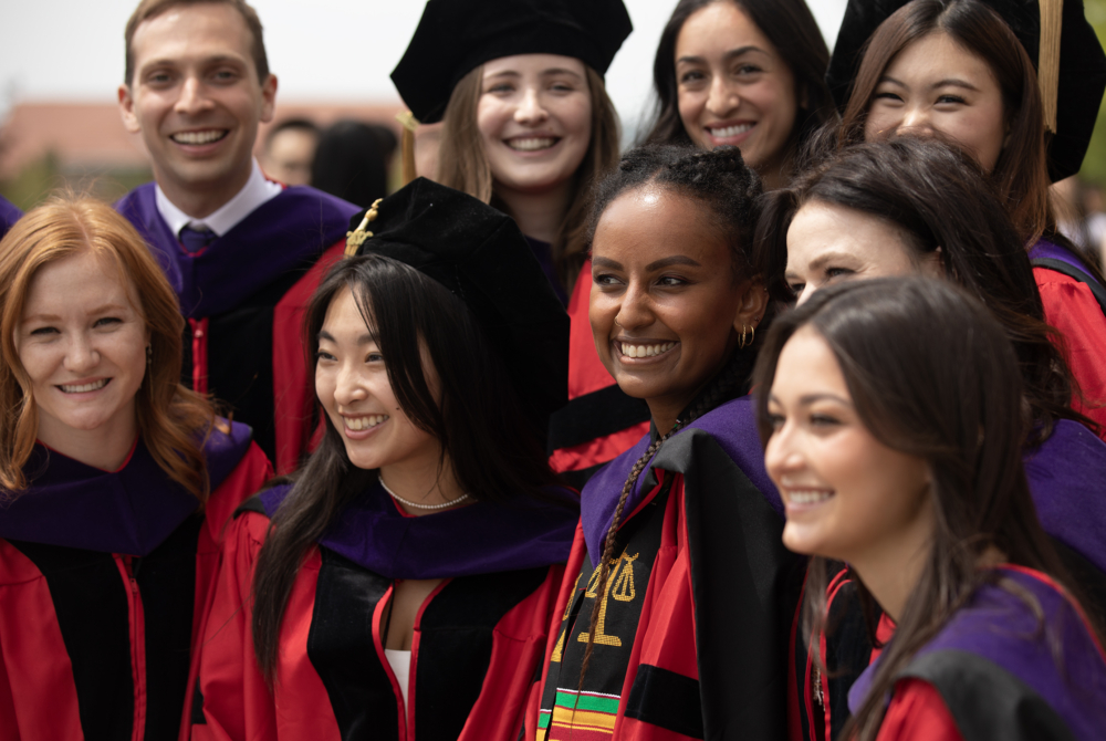 A photo of several students huddled together wearing graduation regalia that is red and black.