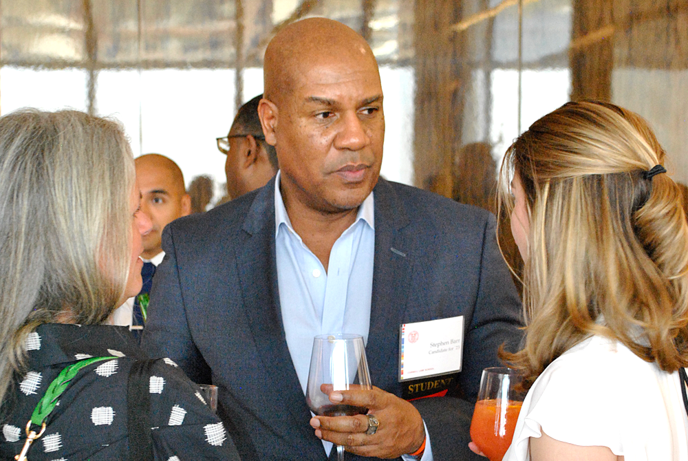Three people are engaged in conversation during a cocktail hour. Two women border a man holding a wine glass who is wearing a suit.