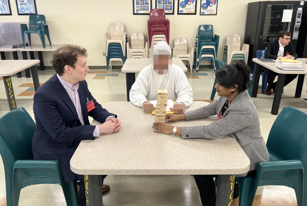 two students and a person playing Jenga in a detention center meeting room