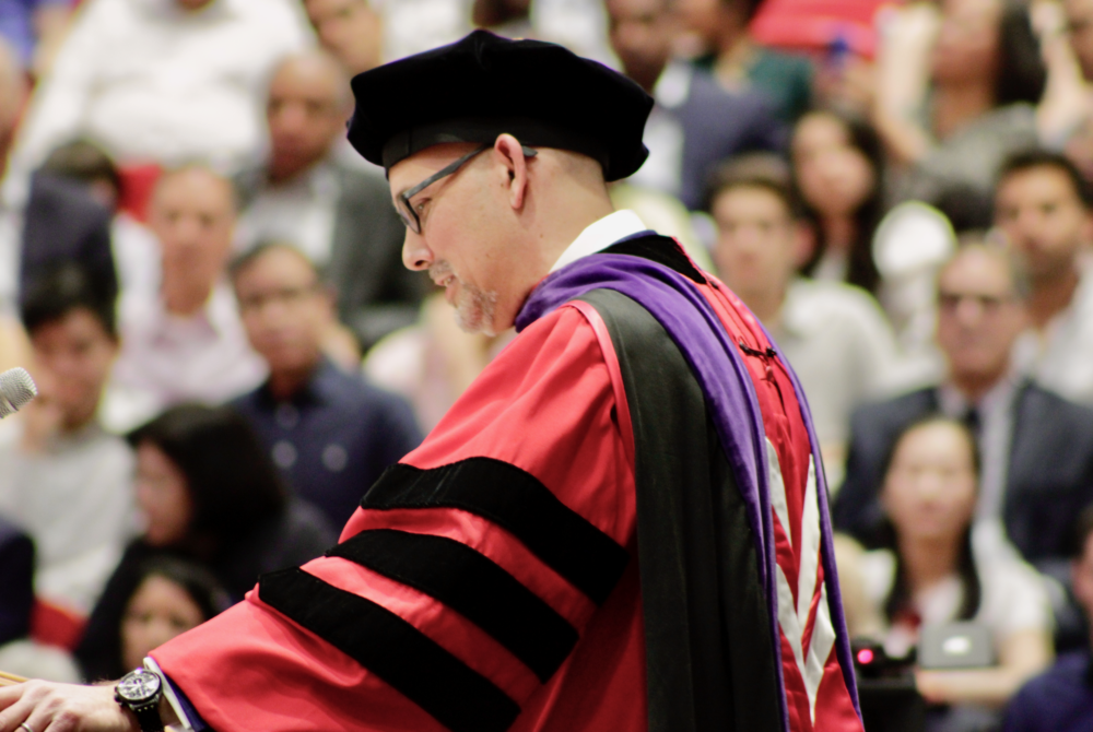 Photo of Dean Jens Ohlin standing at the podium during graduation. The crowd is blurred behind him.