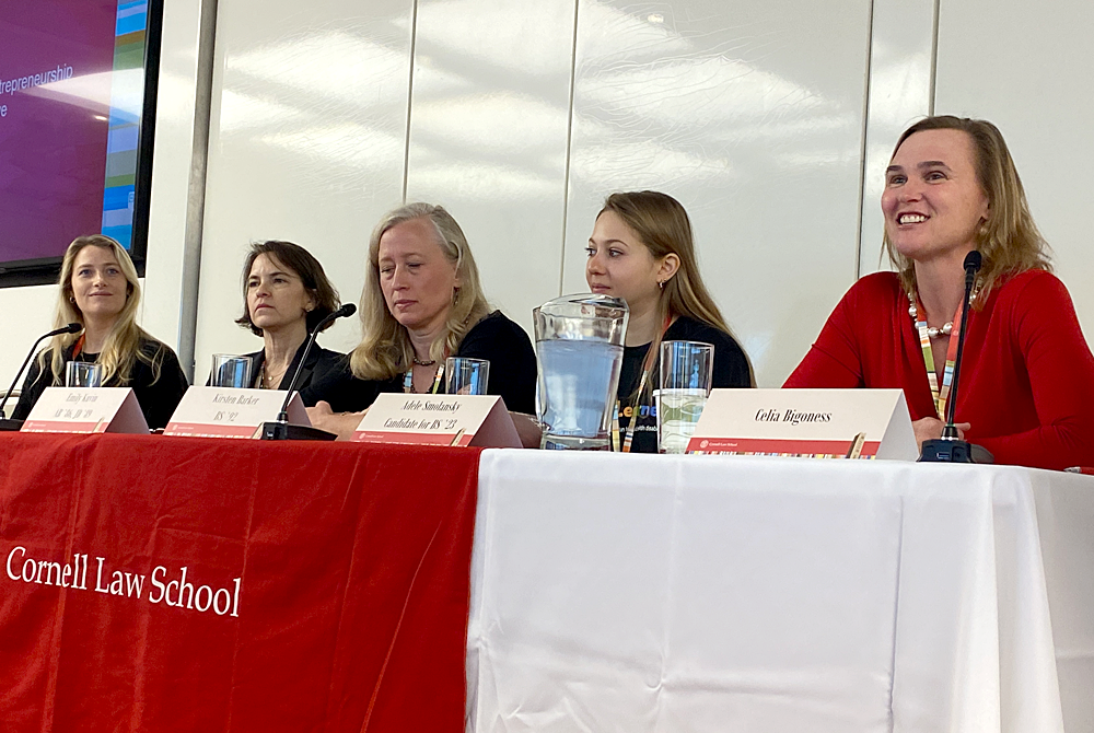 Photo of 5 women sitting behind a long rectangular table with a large, red banner across the front that reads Cornell Law School. The women are panelists and have name table tents in front of them