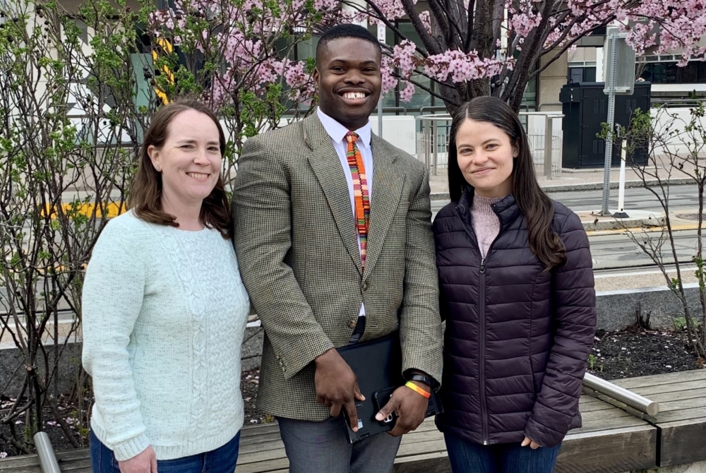 three students in front of a tree with pink blossoms