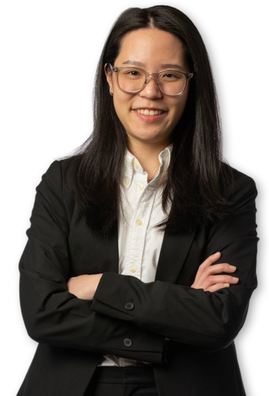 Silo'd photo of a young woman wearing a black suit and crossing her arms. She is wearing glasses and smiling.