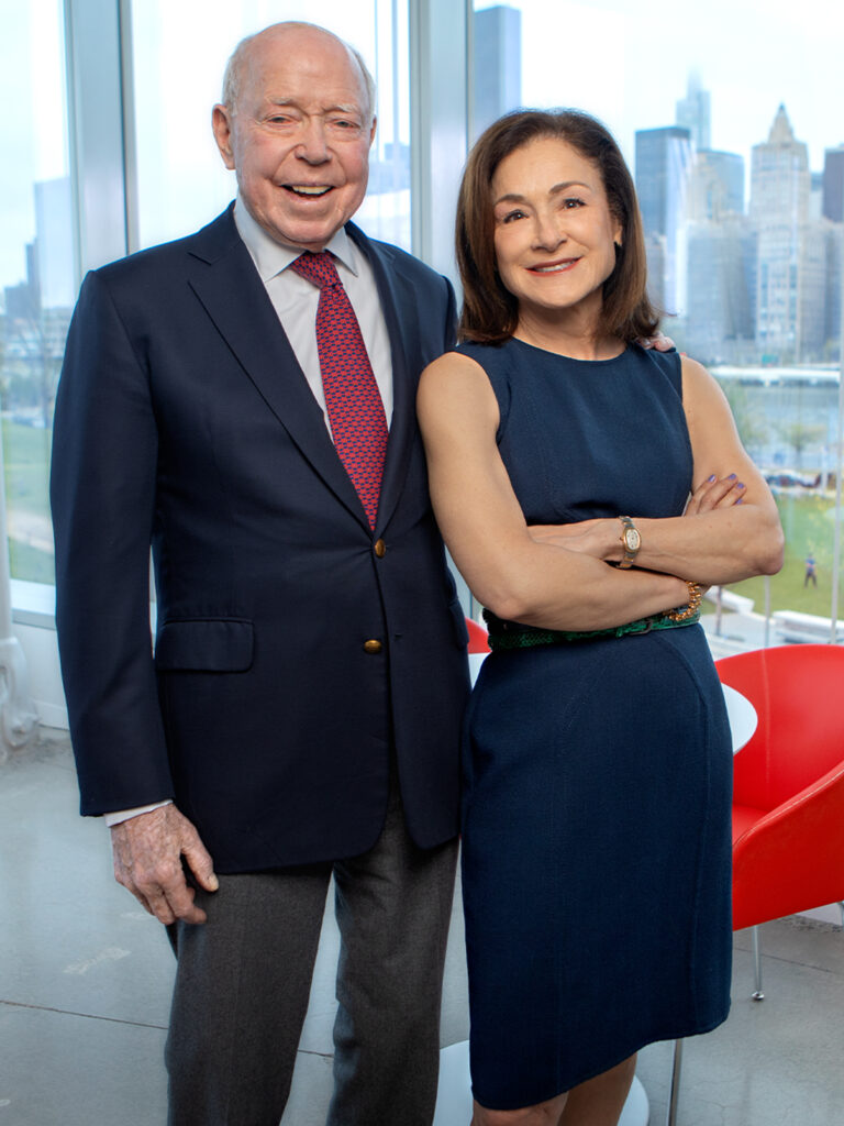 Two people standing side by side with the NYC skyline behind them