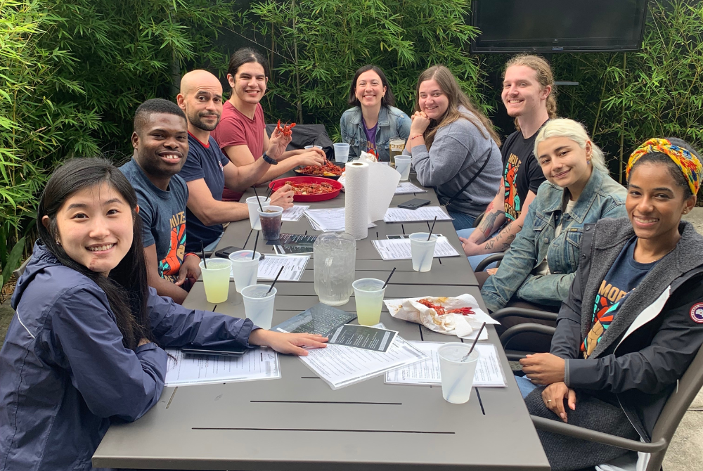 Several students sitting around an outdoor table debriefing their trip with papers in front of them and writing utensils