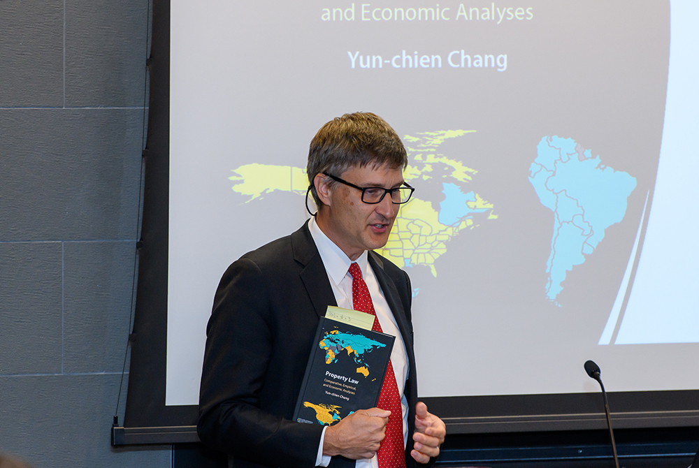 Professor with Professor Chang's book in his hand and a white display screen in the background with event graphics on it.