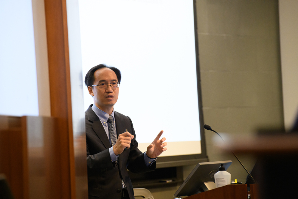 Professor Chang speaking in front of a white screen in the background.