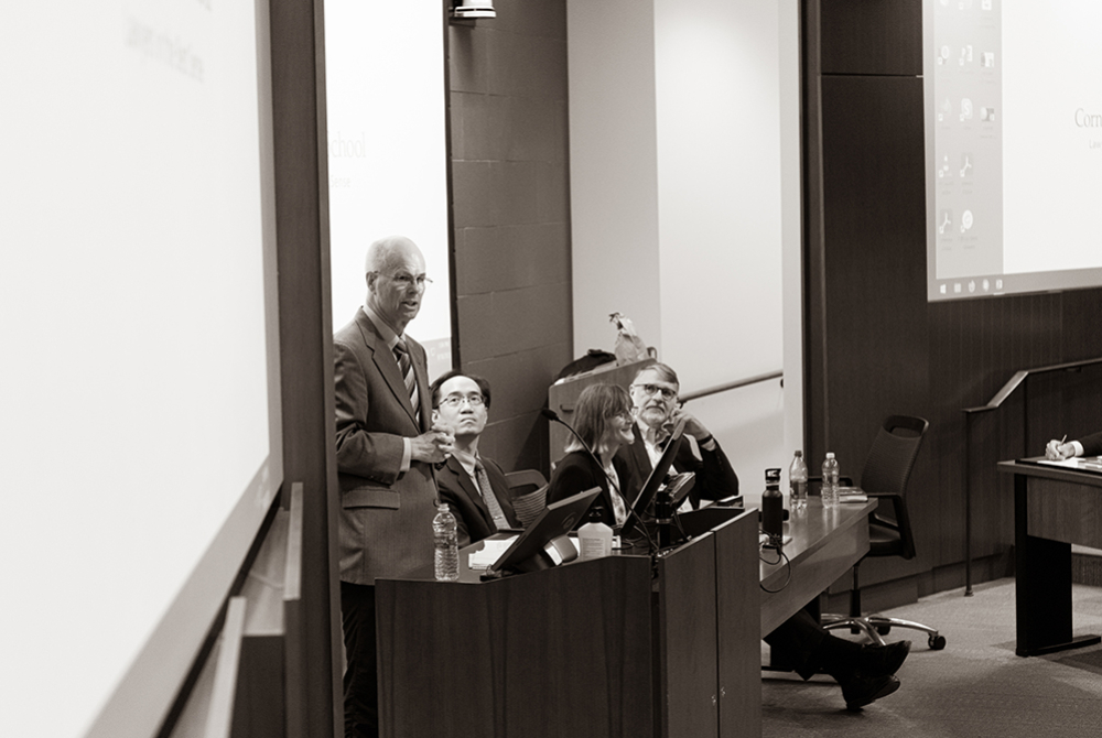 Professor Schwab talking with panelists seated next to him.