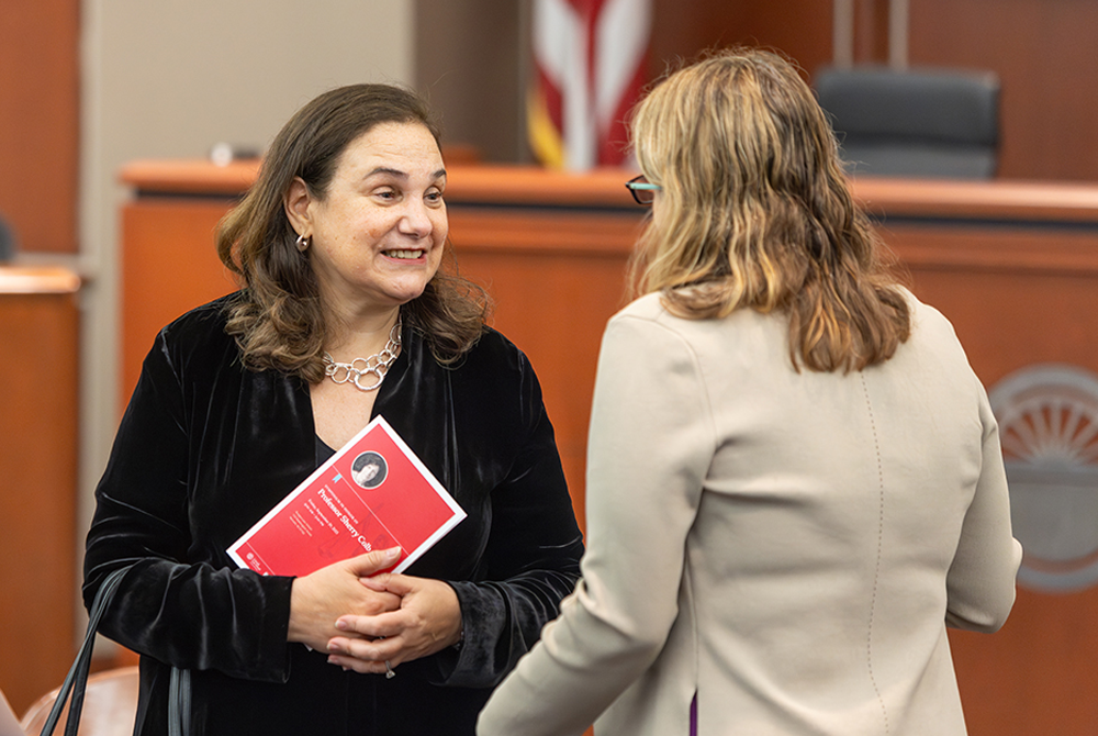 Two attendees at event talking. Attendee on the left is holding a program in her hands.