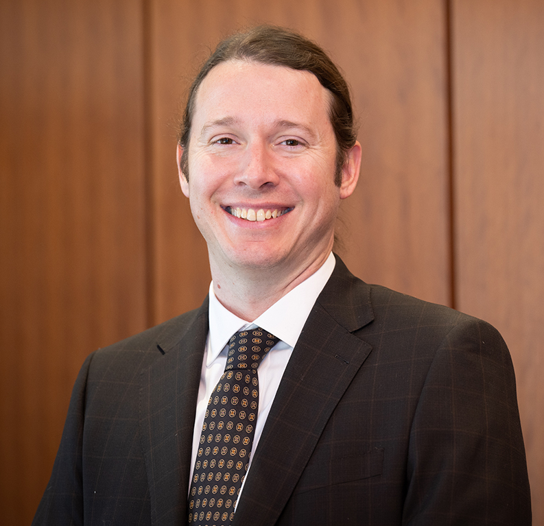 James Hardwick smiling in the foreground with a brown wooden background in the background.