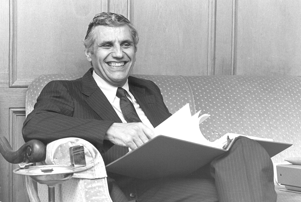photo of Rossi sitting on a polka dot couch, with a folder in his hands, laughing