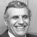 photo of Rossi sitting on a polka dot couch, with a folder in his hands, laughing