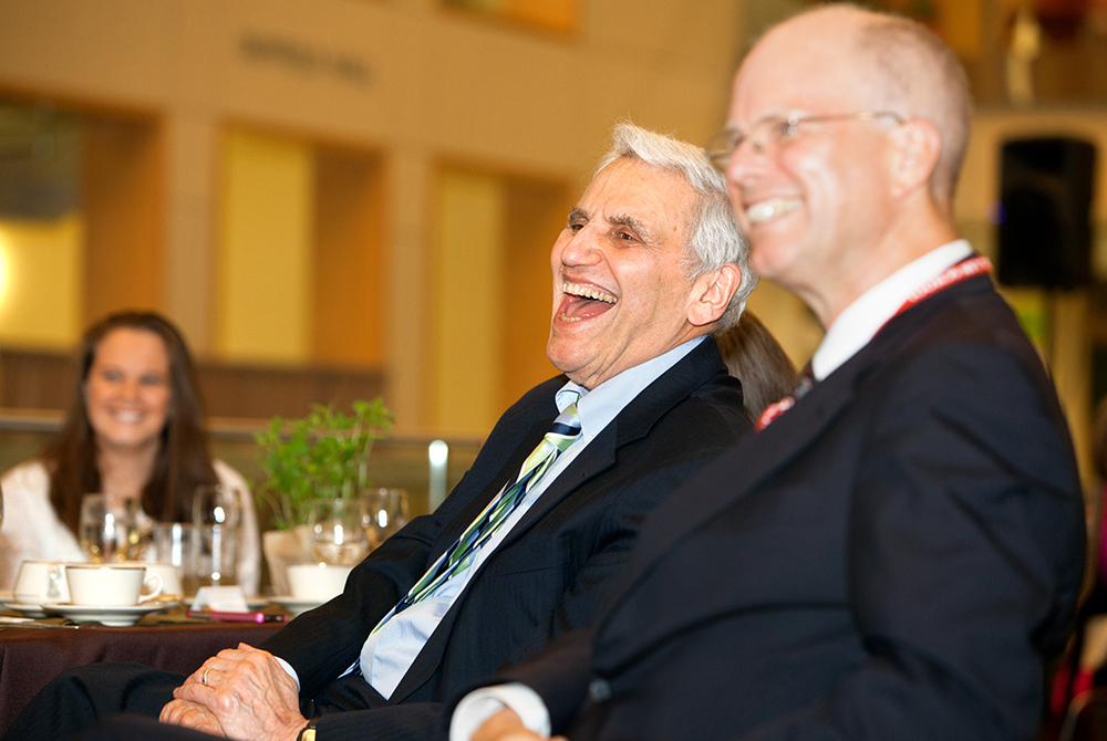 photo of Rossi laughing and sitting next to a man in glasses at an event