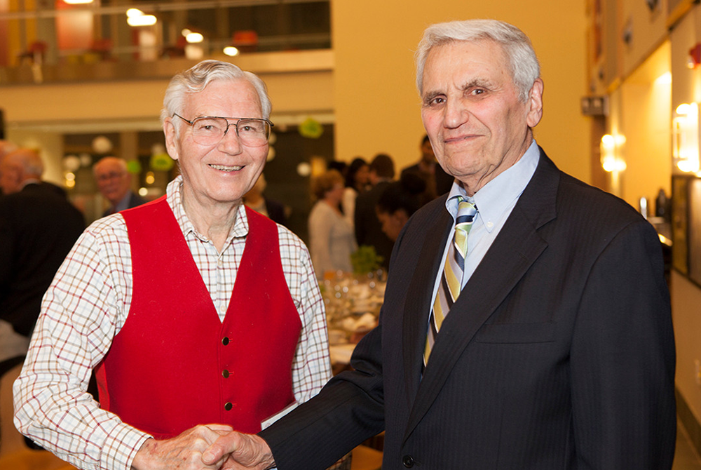 photo of Rossi and a man with glasses in a red sweater, shaking hands at an event