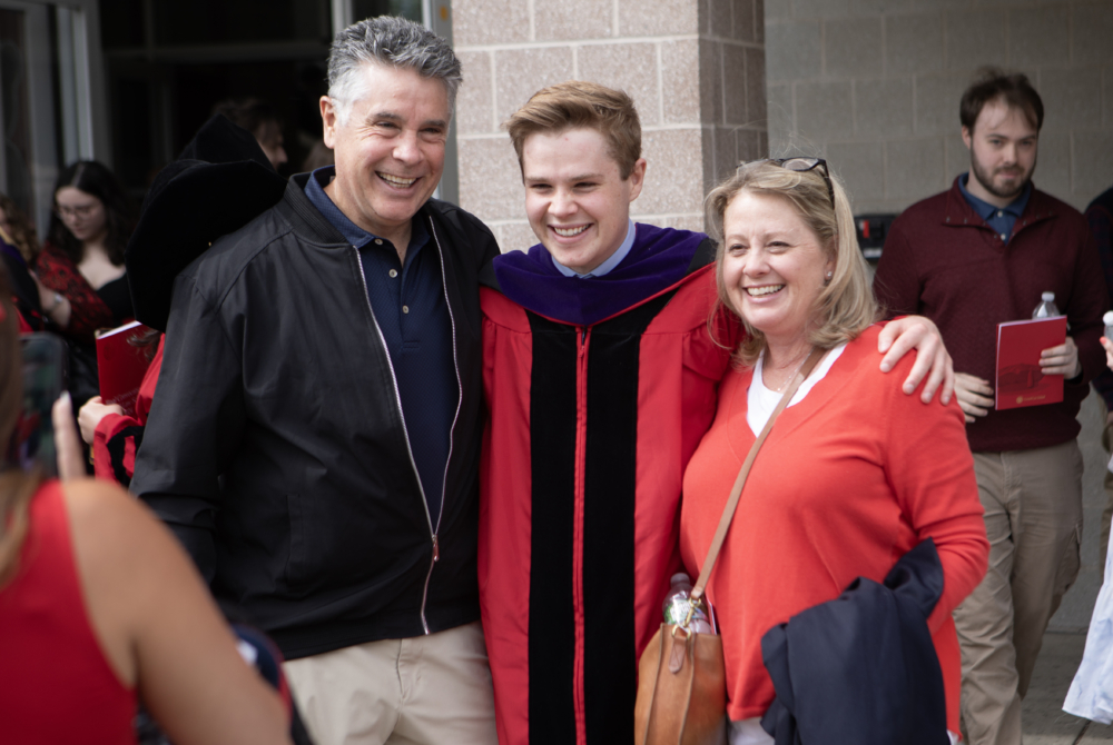 a boy in the middle in his regalia and his two parents on each side of him