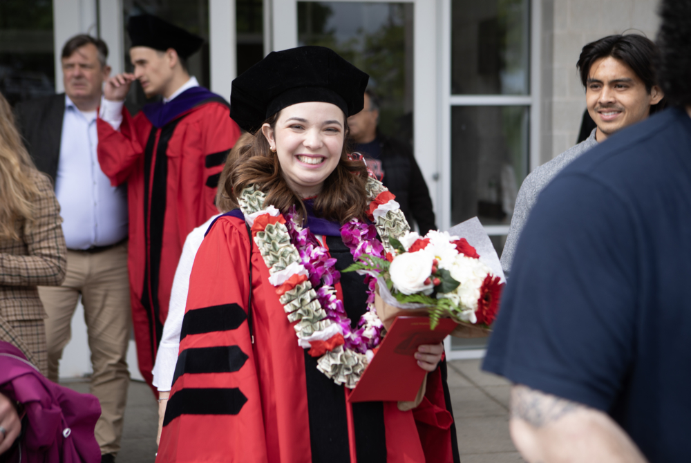a student posing in her regalia with flowers