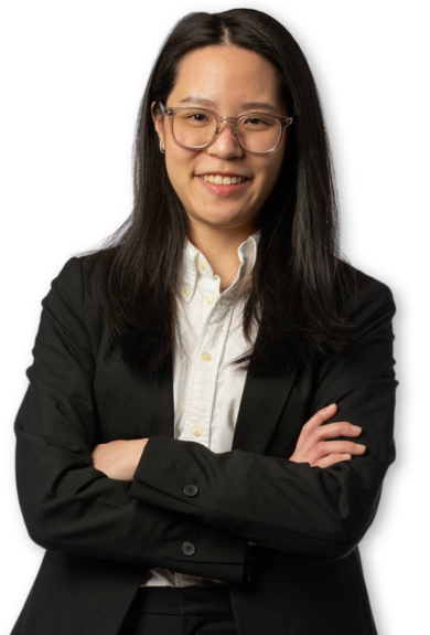 Silo'd photo of a young woman wearing a black suit and crossing her arms. She is wearing glasses and smiling.