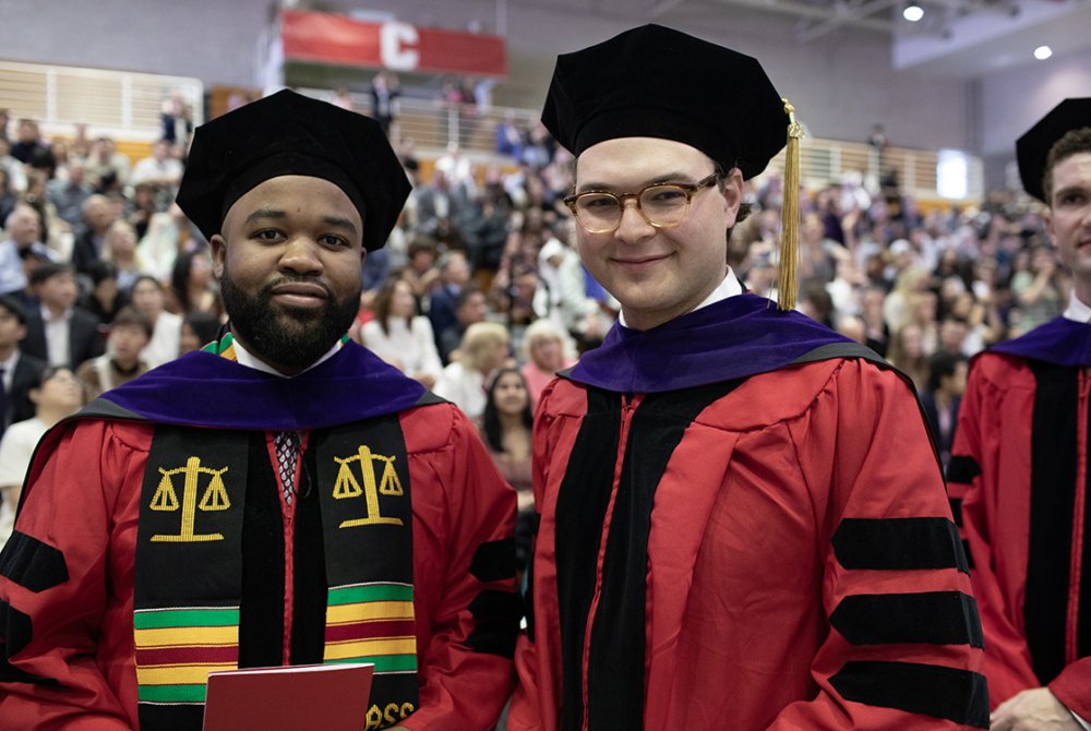 two students standing next to each other in line at graduation posing for a photo