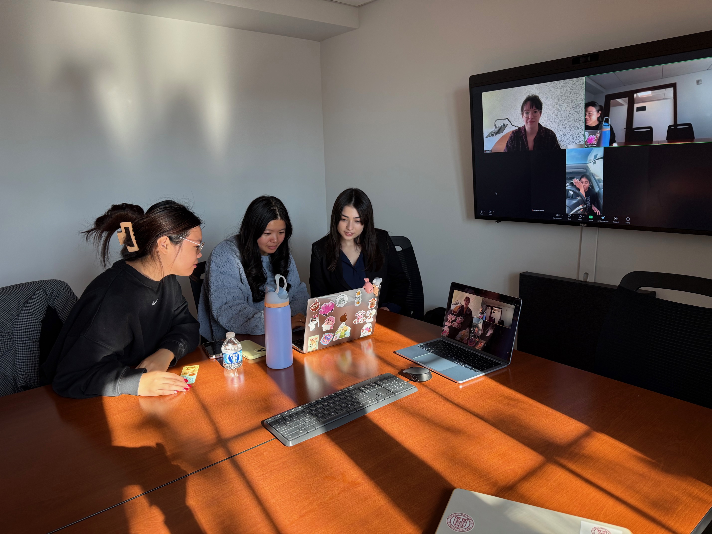 group of students at a table with another group on Zoom on a screen