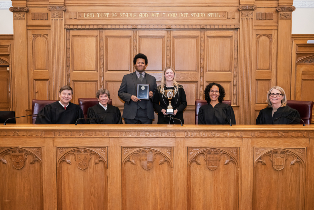 pictured is 2026 rossi moot court competition winner Paxton Trevett and runner up Giovan Soares with trophies and behind them are the judges
