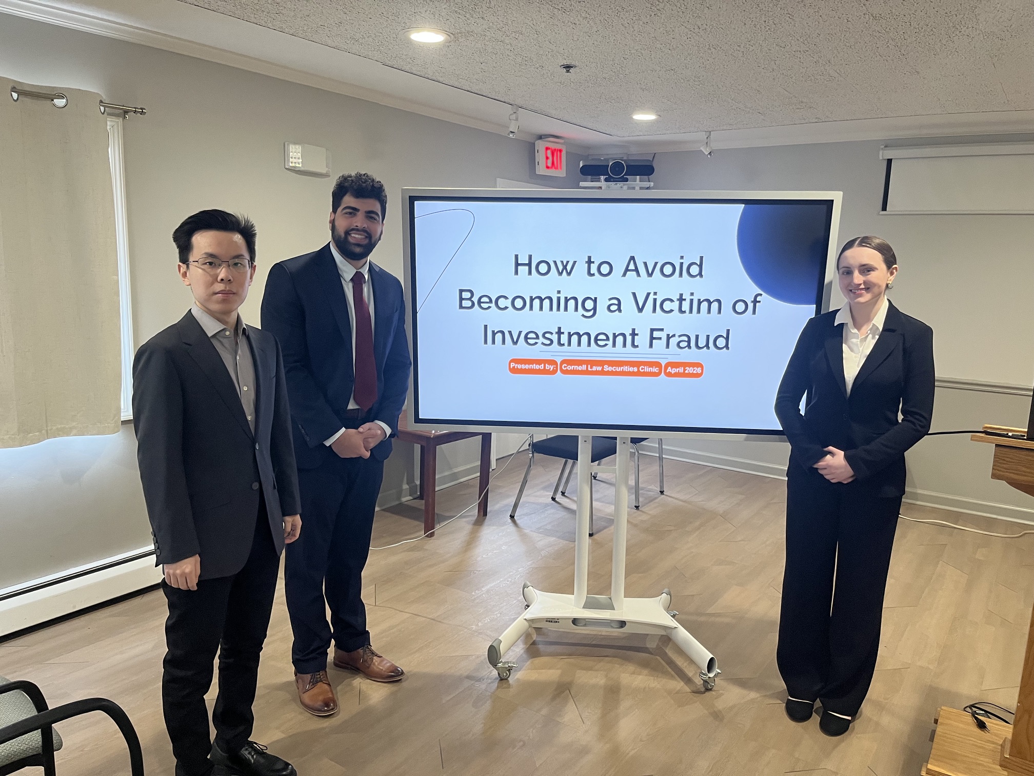 three students in professional attire stand near a monitor